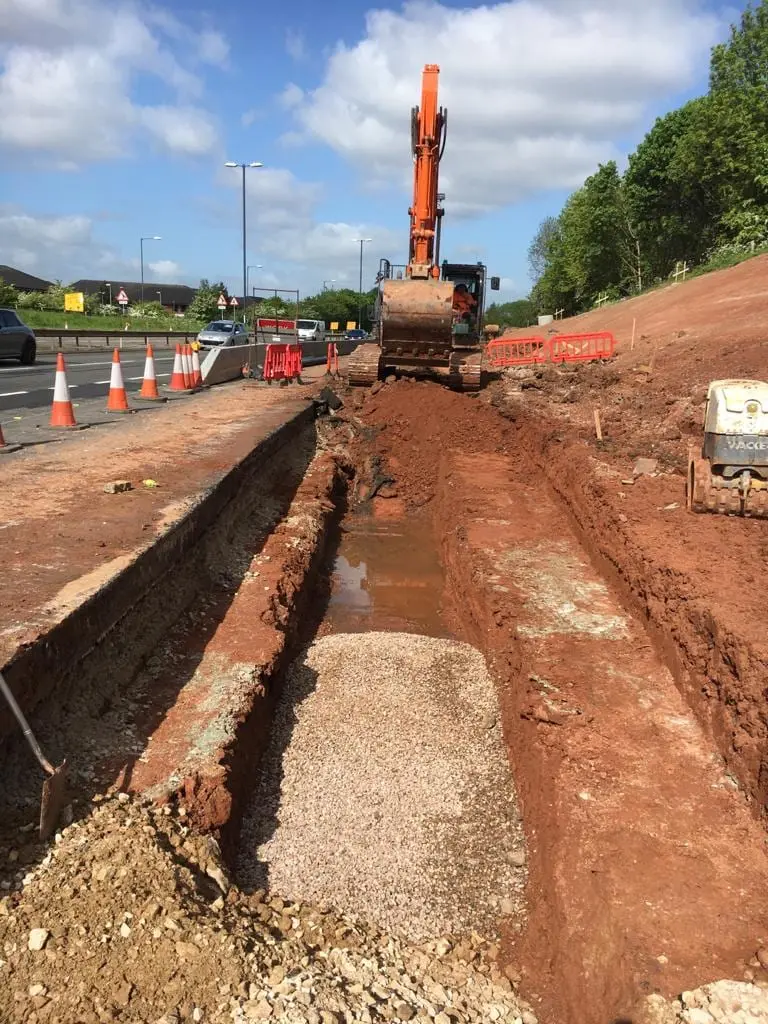 An SMJ Brady excavator cutting a deep service trench alongside a live carriageway