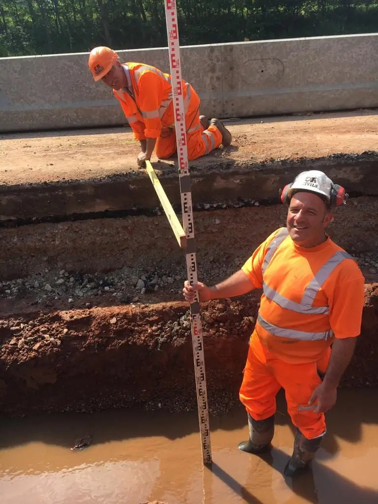 Two SMJ Brady groundworkers setting levels in an open trench